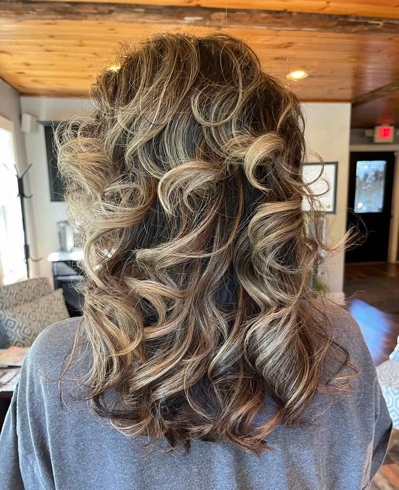 Back view of shoulder-length brunette hair with lighter ribbons, styled in full curls.