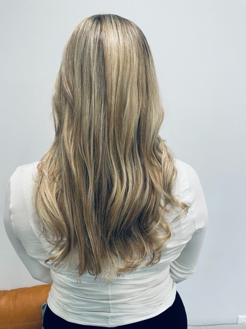 Back view of the same long blonde hair, with a softly blended darker root and loose waves at the ends.