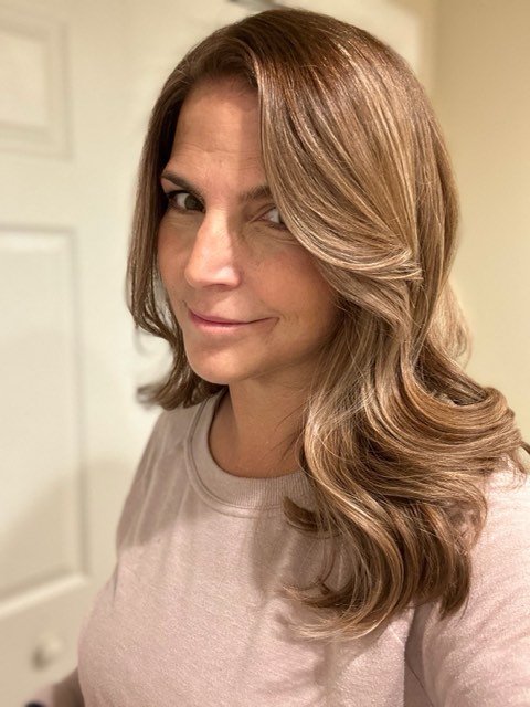 Long brunette hair with lighter bronde ribbons and face-framing layers, styled in a bouncy blowout.