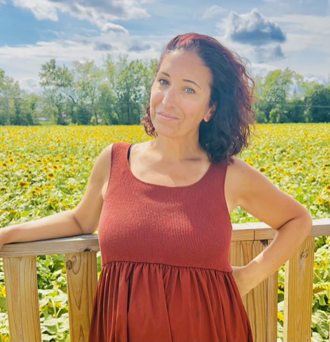 Erica smiling in a sunflower field on a bright summer day.