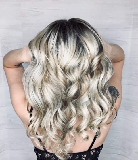 Back view of long icy-blonde hair with a darker root, styled in big, loose curls.